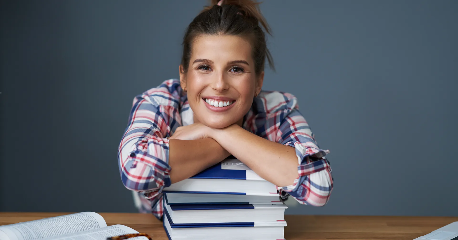 Jonge meid met haar armen op een stapel boeken achter haar bureau